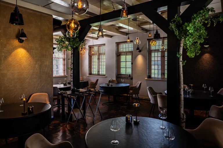 Restaurantinterieur met houten balken, planten en gedekte tafels.