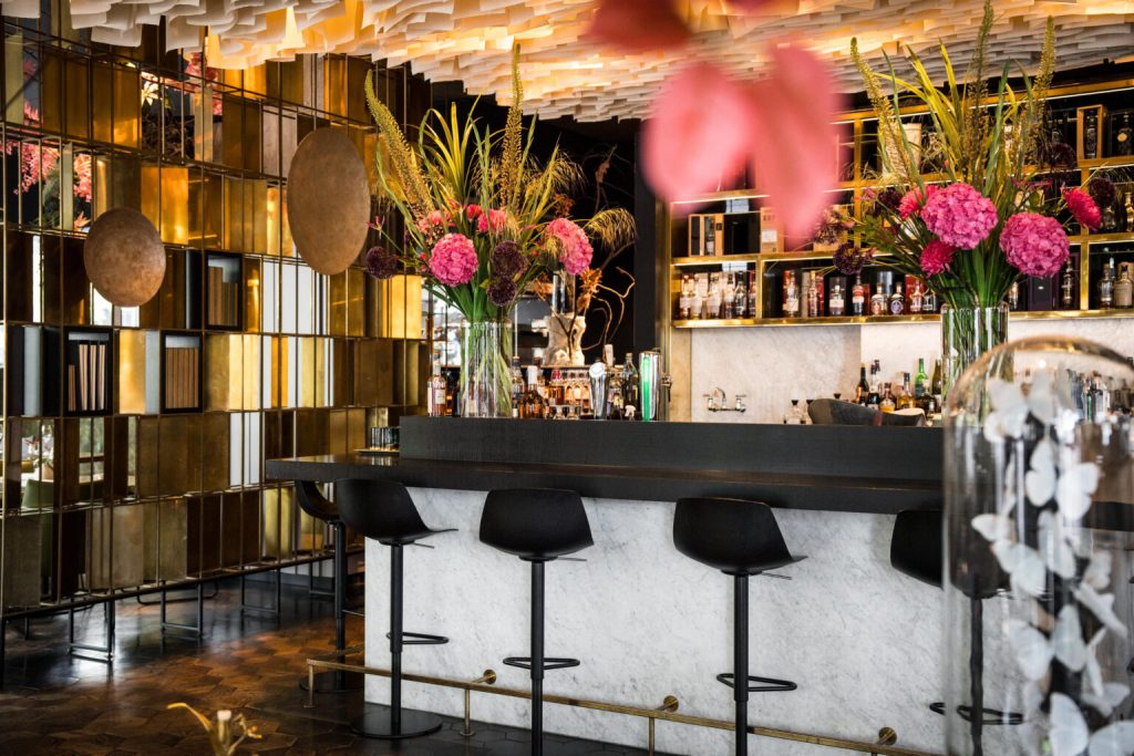 Bar met marmeren balie, bloemen en gouden wanddecoratie.