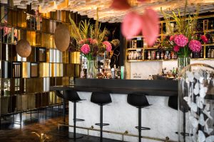 Bar met marmeren balie, bloemen en gouden wanddecoratie.